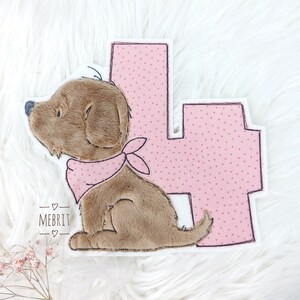 Könnte beinhalten: Ein brauner Plüschwelpe mit einem rosa Halstuch und einer rosa Zahl 4 mit weißen Punkten. Der Welpe befindet sich neben der Zahl 4. Das Wort "MEBRIT" steht darunter.