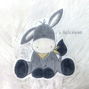 Könnte beinhalten: Ein Plüsch-Esel-Applikation in Grau-, Weiß- und Schwarztönen mit einem gelben Halstuch. Der Esel sitzt mit ausgestreckten Beinen. Der Text "6 Halstuchfarben" und "MEBRIT" ist auf dem Bild.