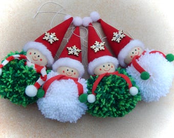 May include: A collection of Christmas ornaments featuring smiling faces, red Santa hats with snowflake accents, and pom-pom bodies. The ornaments have white, green, and red accents, and are strung with white string for hanging.