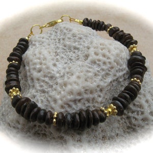 Könnte beinhalten: Ein braunes Holzperlenarmband mit goldenen Akzenten. Das Armband ist aus Naturholz gefertigt und hat ein schlichtes, elegantes Design.