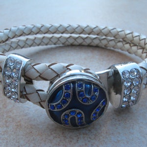 May include: White leather braided bracelet with a silver magnetic clasp. The clasp features a blue enamel circle with silver horseshoe designs and blue rhinestones.