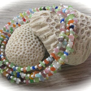 Peut inclure: Collier de perles de verre multicolores avec des perles blanches. Le collier est présenté sur un fond de corail blanc.