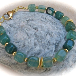 Puede incluir: Un brazalete verde y dorado con cuentas cuadradas. El brazalete tiene un cierre dorado.