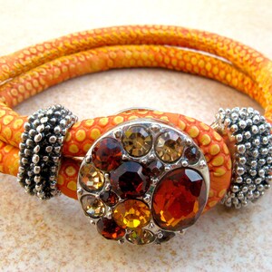 May include: A double-strand orange bracelet with a silver clasp and a round, multi-colored gemstone embellishment.
