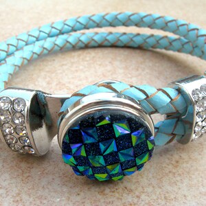 May include: A light blue leather bracelet with a silver clasp and a round, sparkly blue and green button.