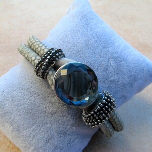 May include: A white leather bracelet with a large, dark blue gemstone and silver accents.