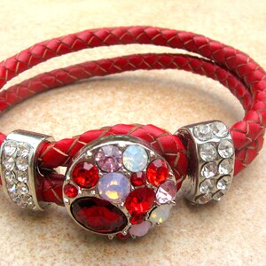 May include: A red leather bracelet with a silver charm featuring a cluster of red, pink, and white rhinestones.