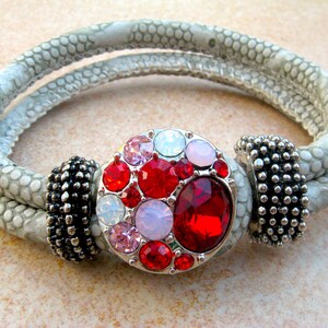 May include: A gray leather bracelet with a silver clasp adorned with red, pink, and white rhinestones.