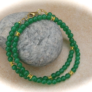 Könnte beinhalten: Ein Armband mit zwei Reihen aus grünen Jadeperlen mit goldenen Akzenten.