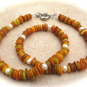 Può includere: Un set di due collane realizzate con perline sovrapposte di colore arancione, giallo e verde. Le collane sono decorate con perle bianche.