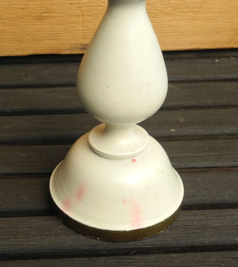 May include: White ceramic candlestick with a gold rim. The candlestick has a bulbous base and a tall, slender stem.