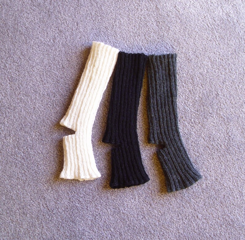 May include: Three pairs of knitted arm warmers, one white, one black, and one dark grey.