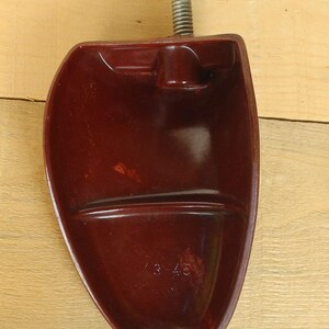 May include: A burgundy shoe stretcher with a metal spring and a curved, foot-shaped form. The number "3-45" is embossed on the bottom of the shoe stretcher. The object is made of a smooth, glossy material.