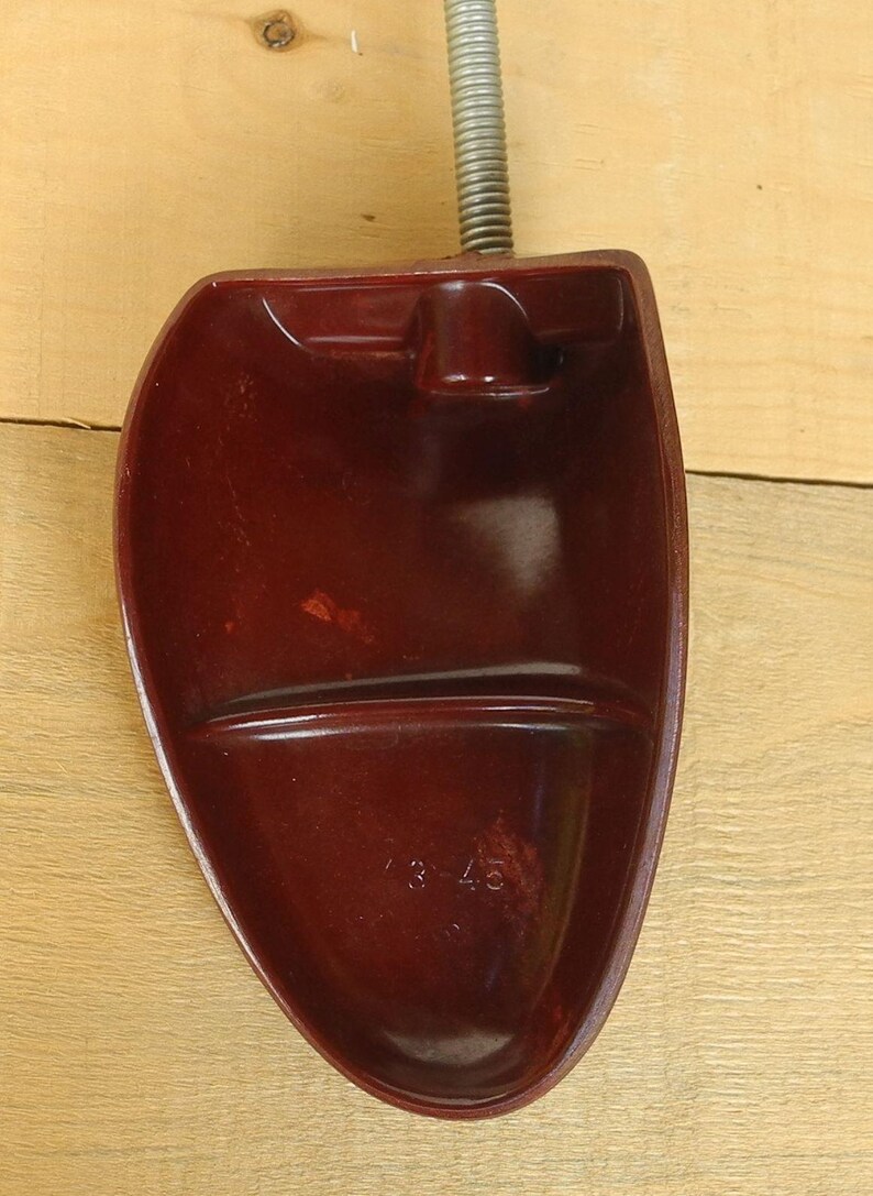 May include: A burgundy shoe stretcher with a metal spring and a curved, foot-shaped form. The number "3-45" is embossed on the bottom of the shoe stretcher. The object is made of a smooth, glossy material.