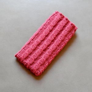 Könnte beinhalten: Ein rechteckiges, handgestricktes Stirnband in einem leuchtenden Pinkton. Das Stirnband hat ein strukturiertes Zopfmuster-Design mit vertikalen Reihen von erhabenen Maschen. Das weiche, warme Accessoire ist perfekt, um die Ohren bei kälterem Wetter warm zu halten.