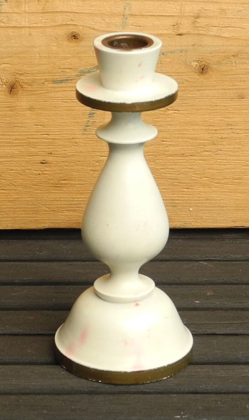 May include: White ceramic candle holder with a gold trim. The holder has a round base and a tall, slender body with a flared top.