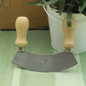 Könnte beinhalten: Ein Mezzaluna-Kräutermesser mit einer gebogenen Metallklinge und zwei hellen Holzgriffen an der Oberseite. Die Zahl 220 ist in die Metalloberfläche der Klinge eingestanzt, was einen klaren Blick auf die Konstruktion des Küchenwerkzeugs ermöglicht.