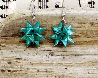 May include: A pair of teal star-shaped earrings featuring a geometric folded design. Each earring hangs from a silver-toned metal hook and includes a small black bead at the base of the star. The star components appear to be crafted from folded paper.