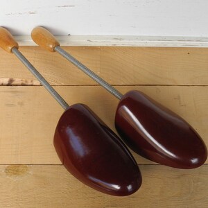 May include: A pair of vintage shoe trees. They have wooden handles and dark burgundy shoe forms. The metal springs connect the handles to the shoe forms. These are designed to maintain the shape of shoes.