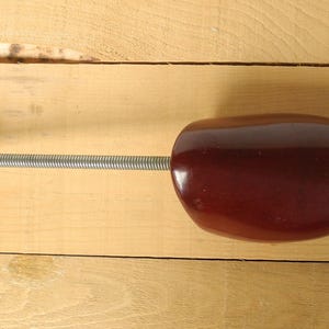 May include: A shoe stretcher, with a dark reddish-brown, oval head and a light-coloured wooden handle. A silver spring connects the head and handle. The shoe stretcher is designed to maintain the shape of shoes.