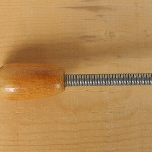 May include: A wooden handle connected to a silver spring. The handle is oval and has a light brown finish. The spring is tightly coiled and extends from the handle.