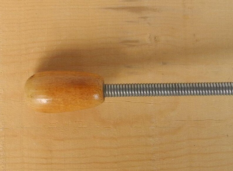 May include: A wooden handle connected to a silver spring. The handle is oval and has a light brown finish. The spring is tightly coiled and extends from the handle.