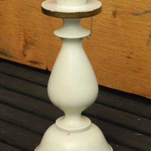 May include: White ceramic candle holder with a gold trim. The holder has a round base and a tall, slender body.