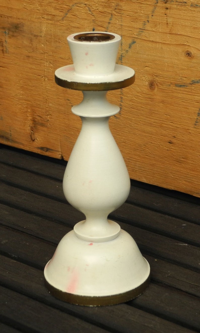 May include: White ceramic candle holder with a gold trim. The holder has a round base and a tall, slender body.