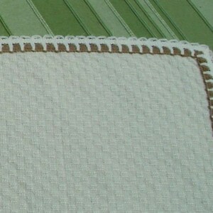 May include: A white crocheted fabric with a brown crocheted border. The fabric has a textured waffle pattern.