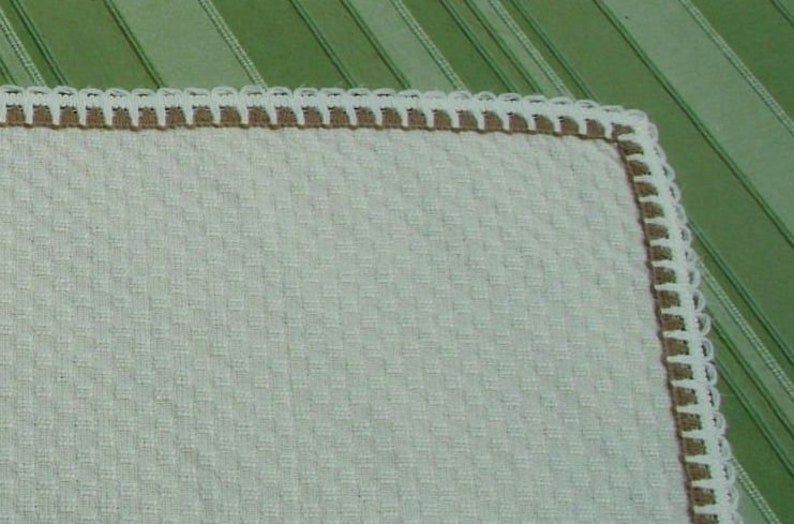 May include: A white crocheted fabric with a brown crocheted border. The fabric has a textured waffle pattern.