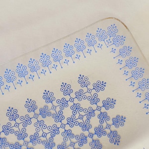 May include: Clear rectangular glass serving dish with a blue floral pattern. The design features stylized blue tree-like shapes arranged in a repeating pattern around the edges and center of the dish. The dish has rounded corners.