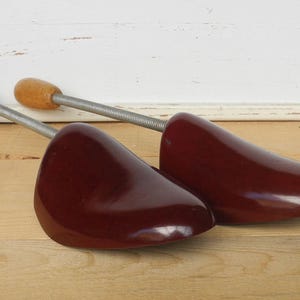 May include: Pair of wooden shoe trees in a dark burgundy finish. The shoe trees feature a spring-loaded design with wooden knobs and metal rods. Designed to maintain the shape of shoes.