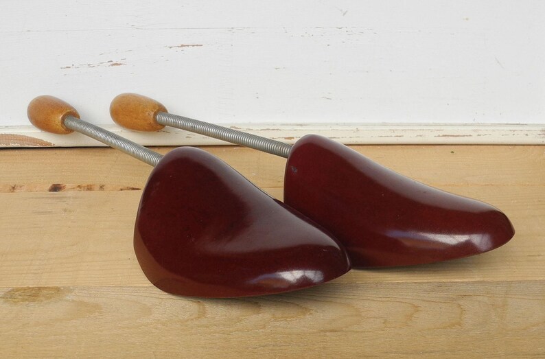 May include: Pair of wooden shoe trees in a dark burgundy finish. The shoe trees feature a spring-loaded design with wooden knobs and metal rods. Designed to maintain the shape of shoes.