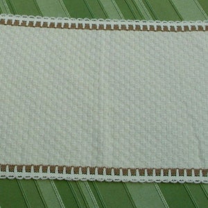 May include: White crocheted table runner with a brown crocheted border. The runner has a textured, woven design.
