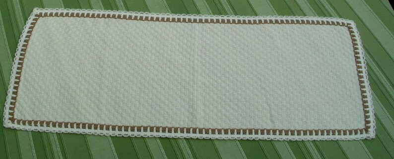 May include: White crocheted table runner with a brown crocheted border. The runner has a textured, woven design.