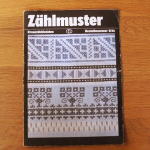 Könnte beinhalten: Ein Vintage-Buch mit dem Titel "ZählMuster" mit Kreuzstichmustern. Das Cover hat einen schwarzen Rand und zeigt verschiedene blaue und weiße Kreuzstichdesigns. Der Titel des Buches ist in fetten weißen Buchstaben geschrieben.