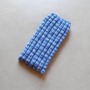 May include: A blue knitted sleeve with a ribbed pattern. The sleeve is a mix of light and dark blue yarns, creating a textured appearance. The item is likely a cozy accessory, possibly for a phone or other small item.