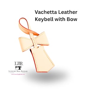 May include: A Vachetta leather keybell with a bow, featuring light beige leather with orange-toned edges and visible stitching. The text "Vachetta Leather Keybell with Bow" is displayed above, and the "LBR Luxury Bag Rehab" logo is at the bottom.