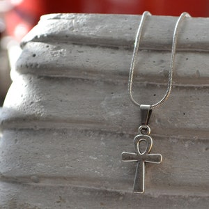 Könnte beinhalten: Eine silberne Kettenkette mit einem Ankh-Anhänger. Der Ankh ist ein Symbol des Lebens in der alten ägyptischen Mythologie.