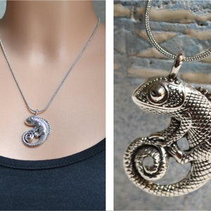 Può includere: Collana con pendente a camaleonte argentato. Il pendente dettagliato, con coda arricciata e pelle strutturata, è sospeso a una sottile catena. La collana è mostrata su uno sfondo scuro, evidenziando il design del gioiello.
