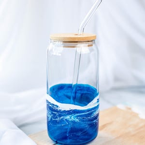K&ouml;nnte beinhalten: Ein Glasgef&auml;&szlig; mit einem blauen und wei&szlig;en Marmormuster, einem Holzdeckel und einem durchsichtigen Glasstrohhalm. Das Gef&auml;&szlig; steht auf einem Holzbrett.