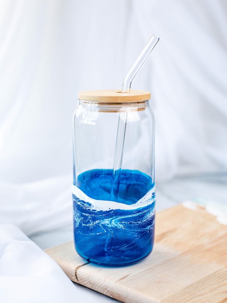 K&ouml;nnte beinhalten: Ein Glasgef&auml;&szlig; mit einem blauen und wei&szlig;en Marmormuster, einem Holzdeckel und einem durchsichtigen Glasstrohhalm. Das Gef&auml;&szlig; steht auf einem Holzbrett.