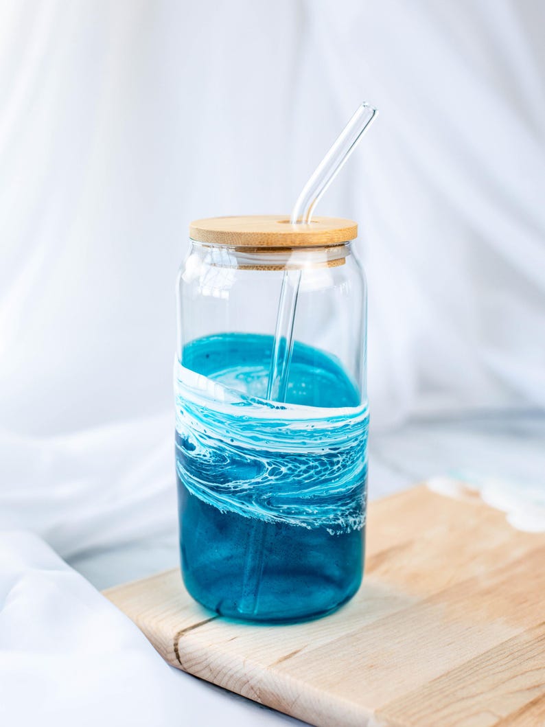 K&ouml;nnte beinhalten: Eine Glaswasserflasche mit einem blauen und wei&szlig;en Wirbelmuster und einem Holzdeckel. Ein Glasstrohhalm befindet sich in der Flasche.