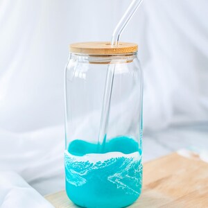 K&ouml;nnte beinhalten: Ein Glas-Trinkglas mit einem t&uuml;rkisblauen und wei&szlig;en Wellendesign. Das Glas hat einen Holzdeckel und einen Glasstrohhalm.
