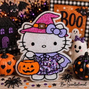 May include: A glittery Hello Kitty figure wearing a pink witch hat and a purple cape, holding an orange jack-o'-lantern bucket. The character features a white face, black whiskers, and a purple bow, accented with purple and silver glitter details.