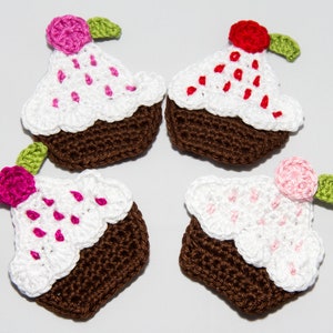 Puede incluir: Cuatro apliques de ganchillo con forma de cupcake, con bases marrones, coberturas blancas con virutas de colores y una pequeña flor con una hoja verde en cada uno. El conjunto incluye una flor rosa, una roja y dos de color rosa claro.