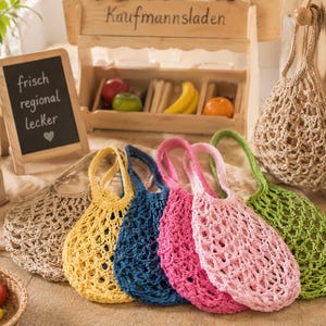 May include: A collection of six reusable string bags in various colors including beige, yellow, dark blue, magenta, light pink, and green. Each bag features a woven net design with two handles, crafted from a textured cord material for carrying items.