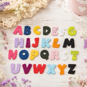 Peut inclure: Un ensemble de vingt-six boutons en bois en forme de lettres de l'alphabet, chacun doté de deux trous pour la couture. Les lettres de A à Z sont présentées dans des couleurs variées, notamment rose, bleu, jaune, noir, violet, rouge, orange, vert et blanc.