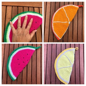 Pode incluir: Quatro pegadores de panela de crochê em forma de fatias de fruta. Os pegadores de panela são melancia, laranja, limão e lima. Os pegadores de panela estão sobre uma superfície de madeira.
