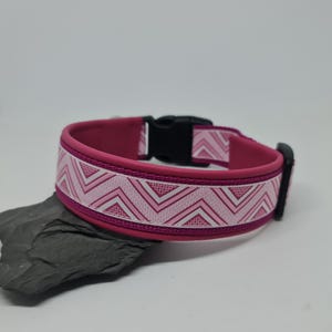 Könnte beinhalten: Ein pinkfarbenes Hundehalsband mit schwarzer Schnalle. Das Halsband hat ein weißes und pinkfarbenes Zickzackmuster auf pinkfarbenem Hintergrund. Das Halsband liegt auf einem dunkelgrauen Stein.
